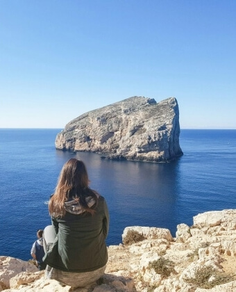 Due persone su una scogliera guardano un grande affioramento roccioso nell'oceano.