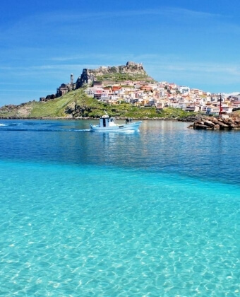 Barca blu e bianca naviga in acque turchesi, con edifici e fortezza sullo sfondo.