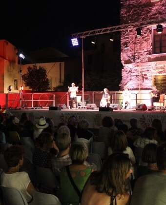 Palco all'aperto di notte con performer, pubblico e luci illuminate.