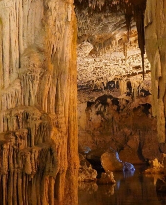 Caverna con stalattiti e stalagmiti, acqua riflettente sul pavimento.