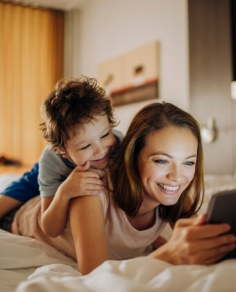 Donna e bambino guardano un tablet sdraiati su un letto.