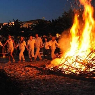 Falò luminoso con persone in bianco danzando in cerchio.