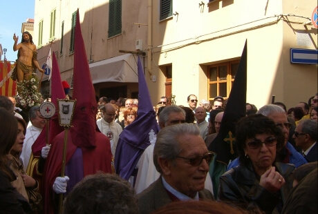 Processione con statue, persone in cappucci e croce rossa.