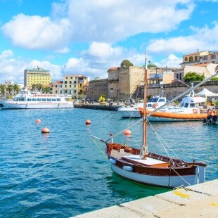 Porto con barche, edifici vari e cielo blu con nuvole.
