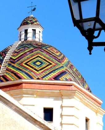 Colorful dome with diamond tiles and weather vane against blue sky. Dome colorato con piastrelle a diamante e banderuola nel cielo blu.