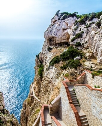 Scogliera ripida con scala in pietra che scende verso l'oceano blu.