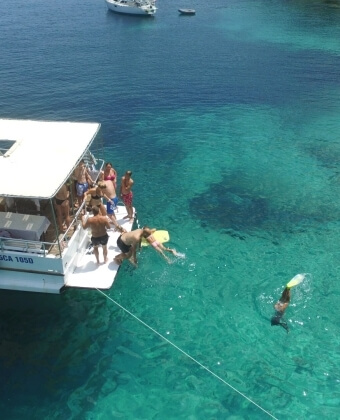 Barca bianca con persone, qualcuno salta in acqua, altri nuotano.