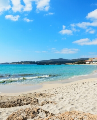 Spiaggia sabbiosa con acqua turchese e edificio con tetto arancione.