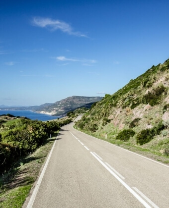 Strada curvilinea accanto a una collina verde e acqua distante.