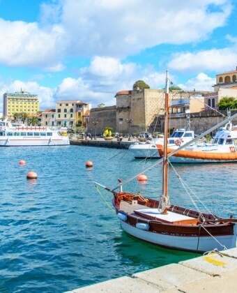 Porto con barche, edifici e cielo blu con nuvole bianche.