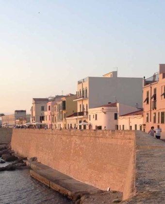 Muro di pietra lungo l'acqua con persone e edifici colorati dietro.