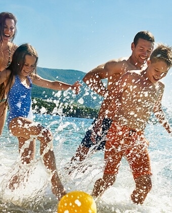 Una famiglia gioca nell'oceano, calciando una palla gialla.