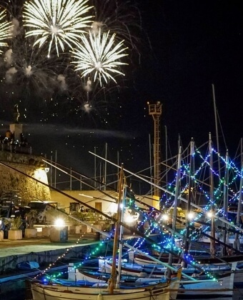Porto notturno con barche illuminate e fuochi d'artificio nel cielo.