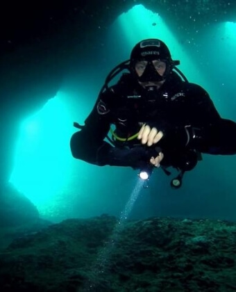 Subacqueo in tuta nera illumina una caverna con una torcia.