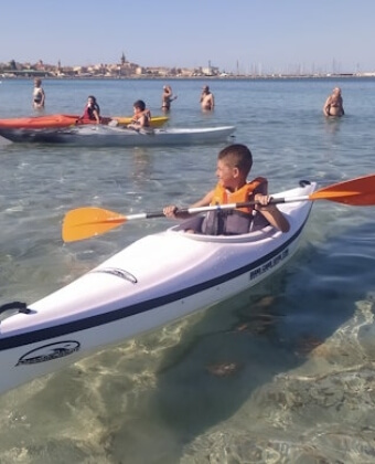 Giovane in kayak bianco con giubbotto arancione su acqua chiara.