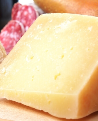Fetta di formaggio giallo chiaro con salame a fette dietro.