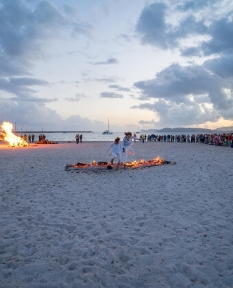 Due persone in bianco camminano su una linea di fuoco sulla spiaggia.