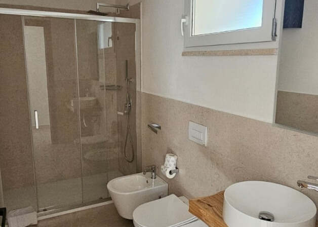 Bagno d'hotel con bidet, doccia, lavabo e pareti in pietra.