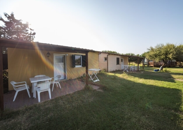 Due bungalow con patio, tavolo bianco e sedie, circondati da alberi.