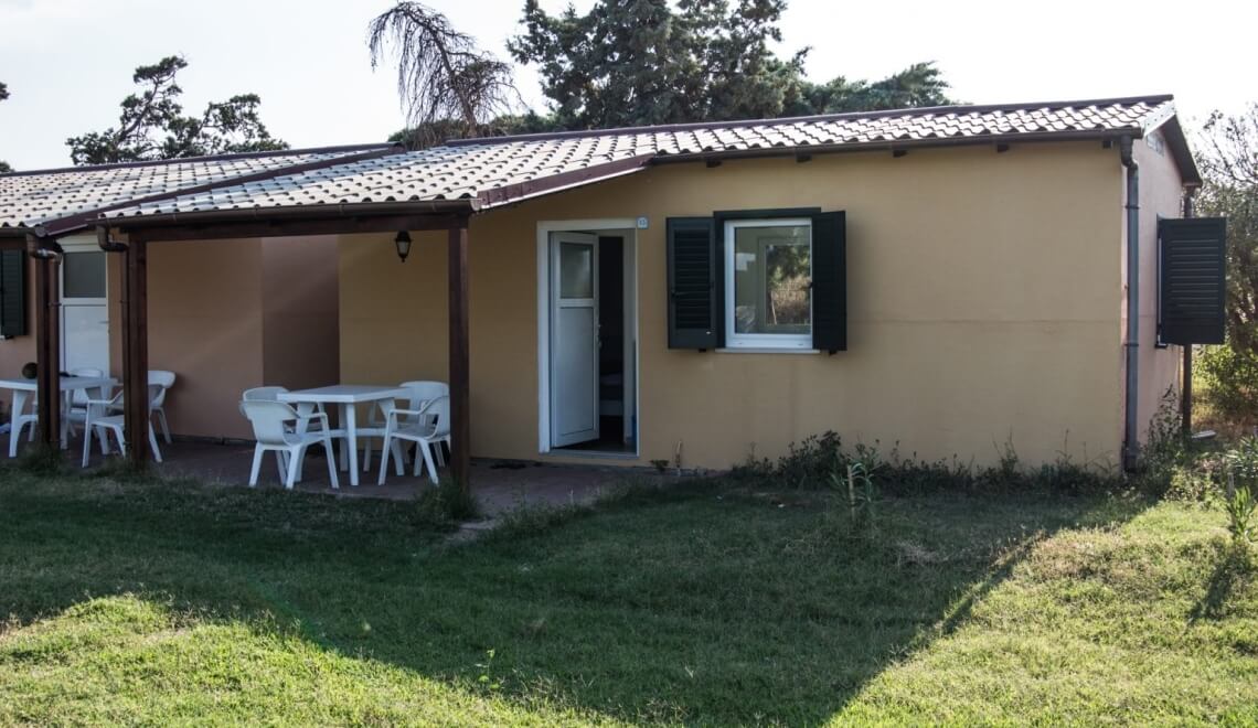Edificio con patio coperto, tavoli bianchi e giardino verde.