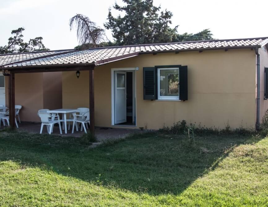 Piccola costruzione con patio, tavolo, sedie e finestre verdi.