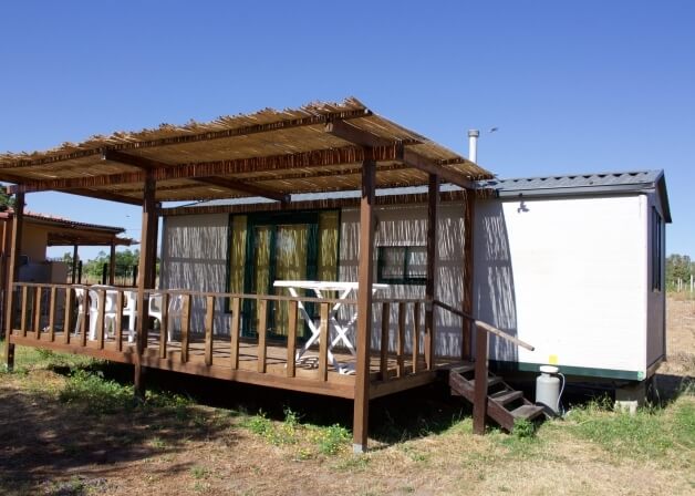 Deck with thatched roof, white furniture, and green doors.