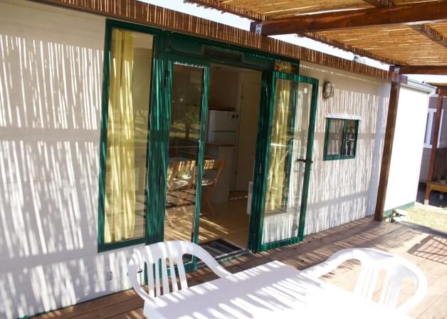 Mobile home entrance with green doors, wooden deck, and kitchen visible.   Entrata della casa mobile con porte verdi e cucina visibile.