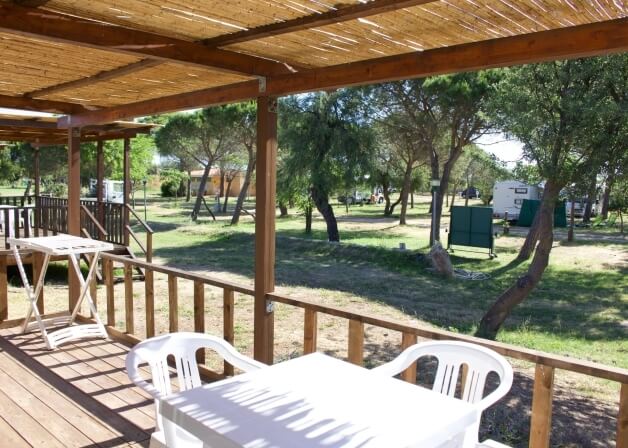 Deck with white tables, chairs, and mobile homes in background.   **Italian:** Terrazza con tavoli bianchi e case mobili sullo sfondo.