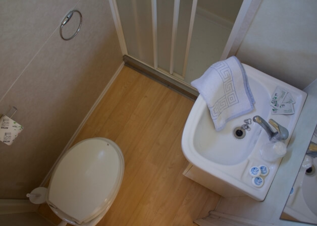 Bagno piccolo con lavabo, doccia, WC e asciugamano piegato.