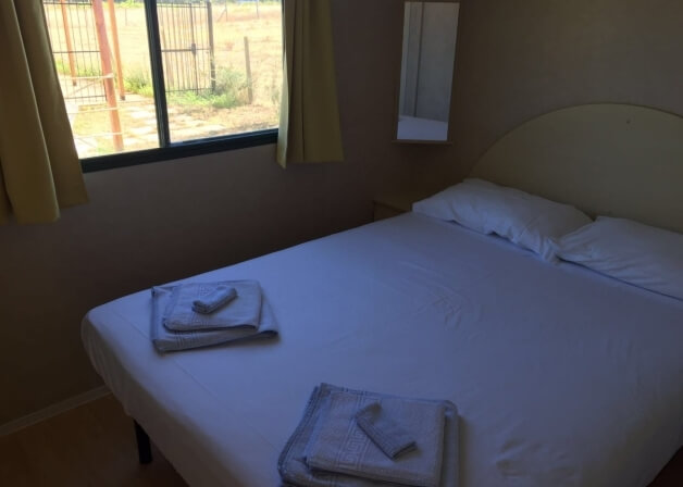 Camera d'hotel con letto bianco, asciugamani piegati e finestra.