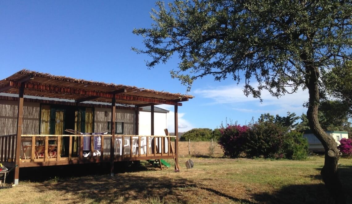 Bungalow con deck in legno, lavanderia e caravan sullo sfondo.