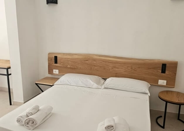 Camera d'hotel con letto bianco, tavolo e scrivania in legno.