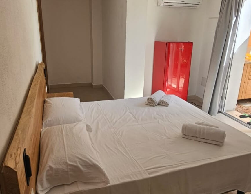 Camera d'hotel con letto, frigorifero rosso e tende grigie.