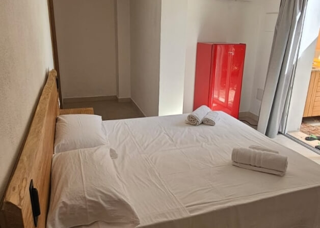 Camera d'hotel con letto bianco, frigorifero rosso e asciugamani.