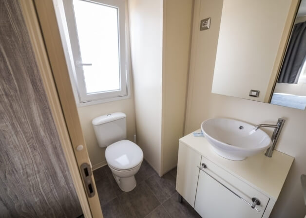 Bagno con toilet, lavabo, vanità, specchio e finestra bianca.