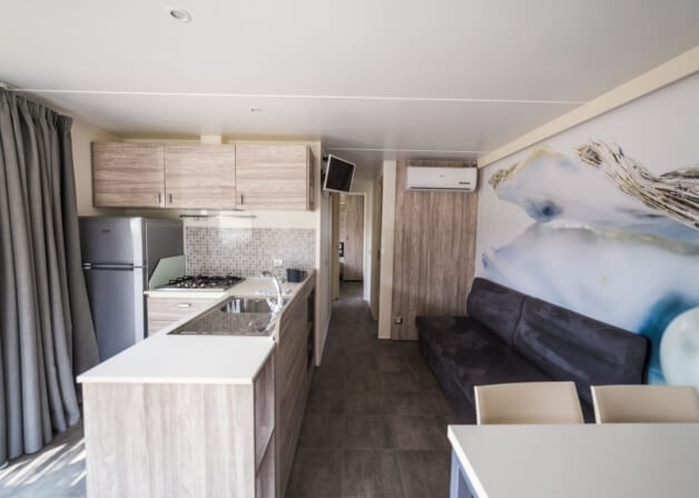 Cucina moderna con soggiorno, divano scuro e murale naturale.