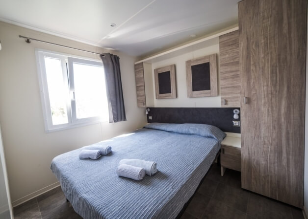 Camera con letto a strisce blu, asciugamani bianchi e finestre.