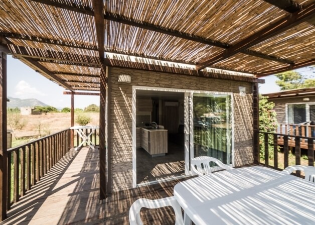 Deck with thatched roof, stone building, and kitchen visible inside.   **Italian:** Terrazza con tetto di paglia, edificio in pietra e cucina visibile.