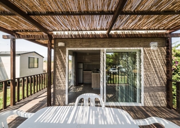 Deck with thatched roof, plastic furniture, and mobile home view.   Deck con tetto di paglia, mobili in plastica e vista sulla casa mobile.