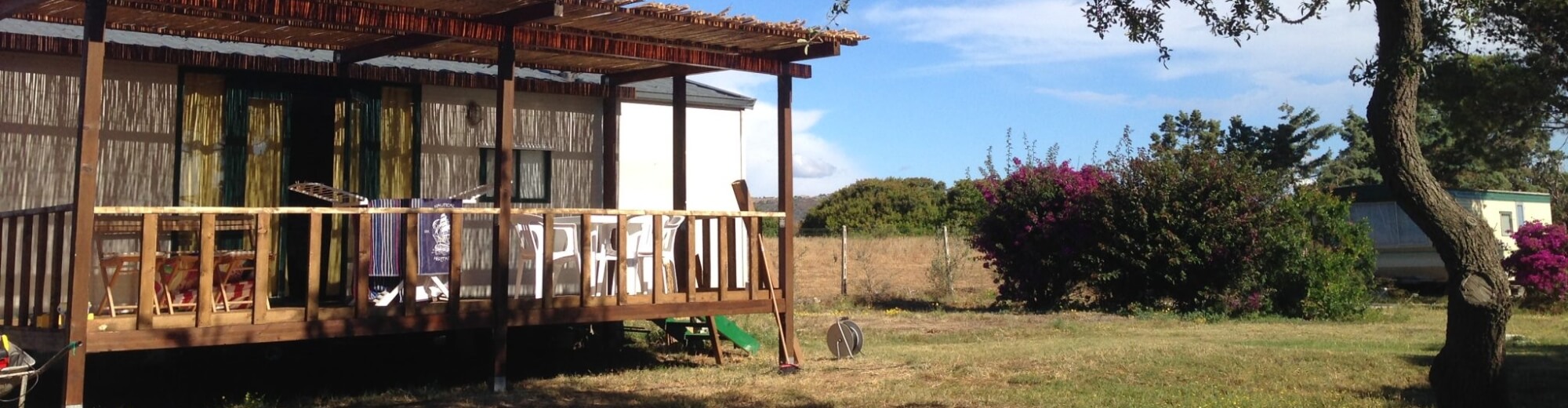Mobile home with wooden deck, chairs, and drying rack.