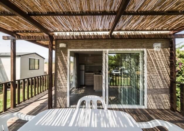 Area esterna con tavolo bianco, sedie e tetto di paglia.