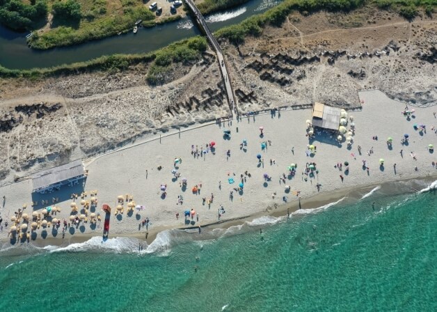 Spiaggia affollata con ombrelloni colorati e persone in acqua.