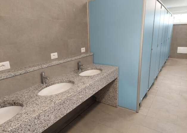 Bagno pubblico con lavandini, porte blu e parete grigia.