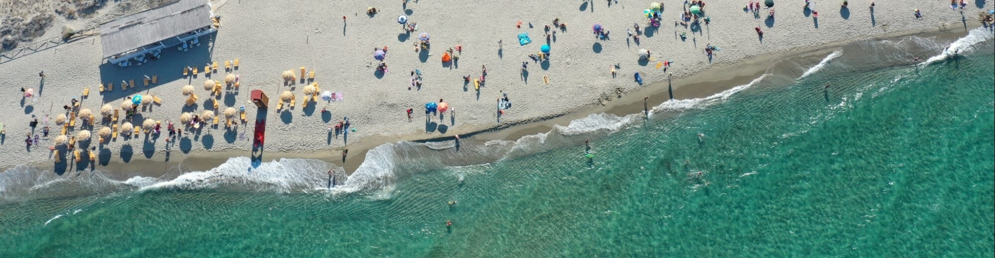 Vista aerea di una spiaggia affollata con ombrelloni e onde.