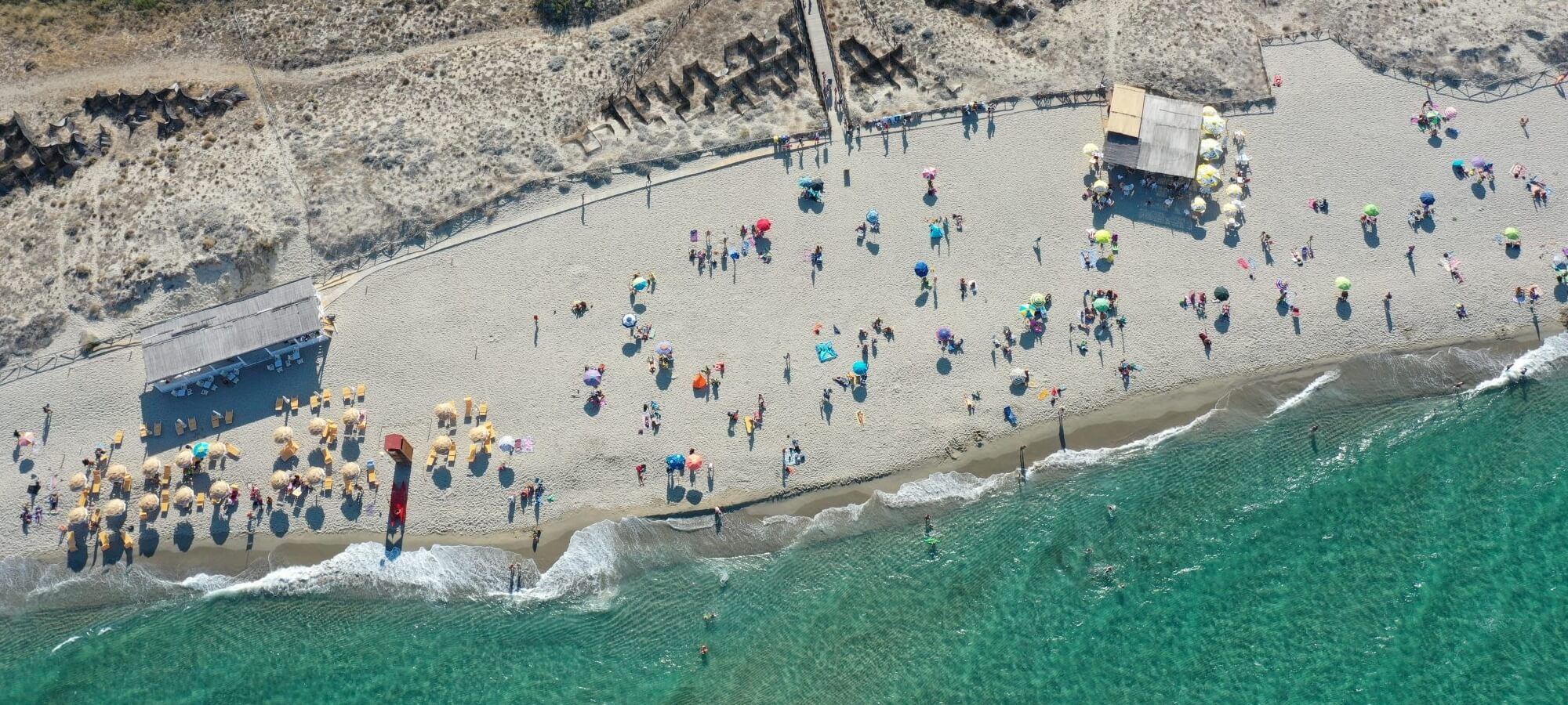 Vista aerea di una spiaggia sabbiosa con ombrelloni e persone.