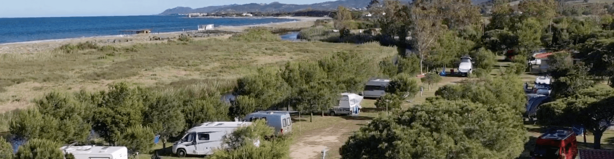 Campeggio con camper e roulotte vicino a un lago e colline.