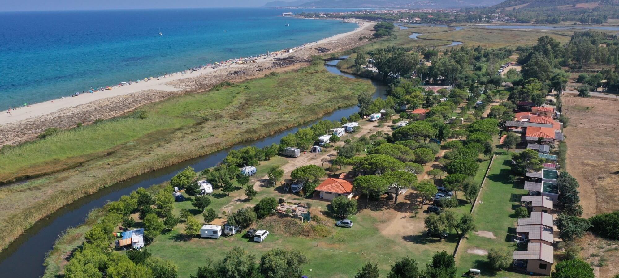 Paesaggio costiero con spiaggia, vegetazione, edifici e campeggio.