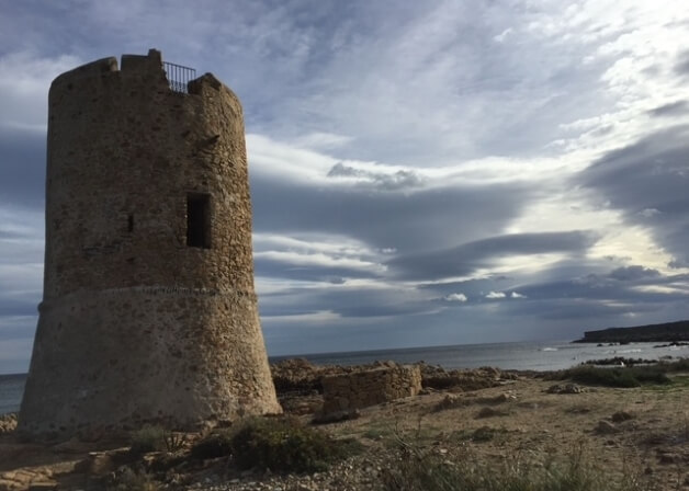Torre di pietra cilindrica su una costa rocciosa, cielo nuvoloso.