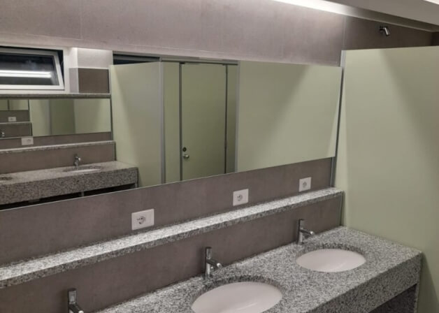 Bagno pubblico con lavabo in granito, specchio grande e prese elettriche.
