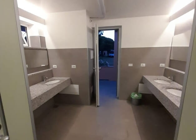 Bagno comune con doppi lavandini, porta aperta e finestra.